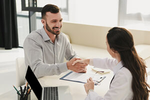 smiling client shaking hands with doctor in office with laptop a